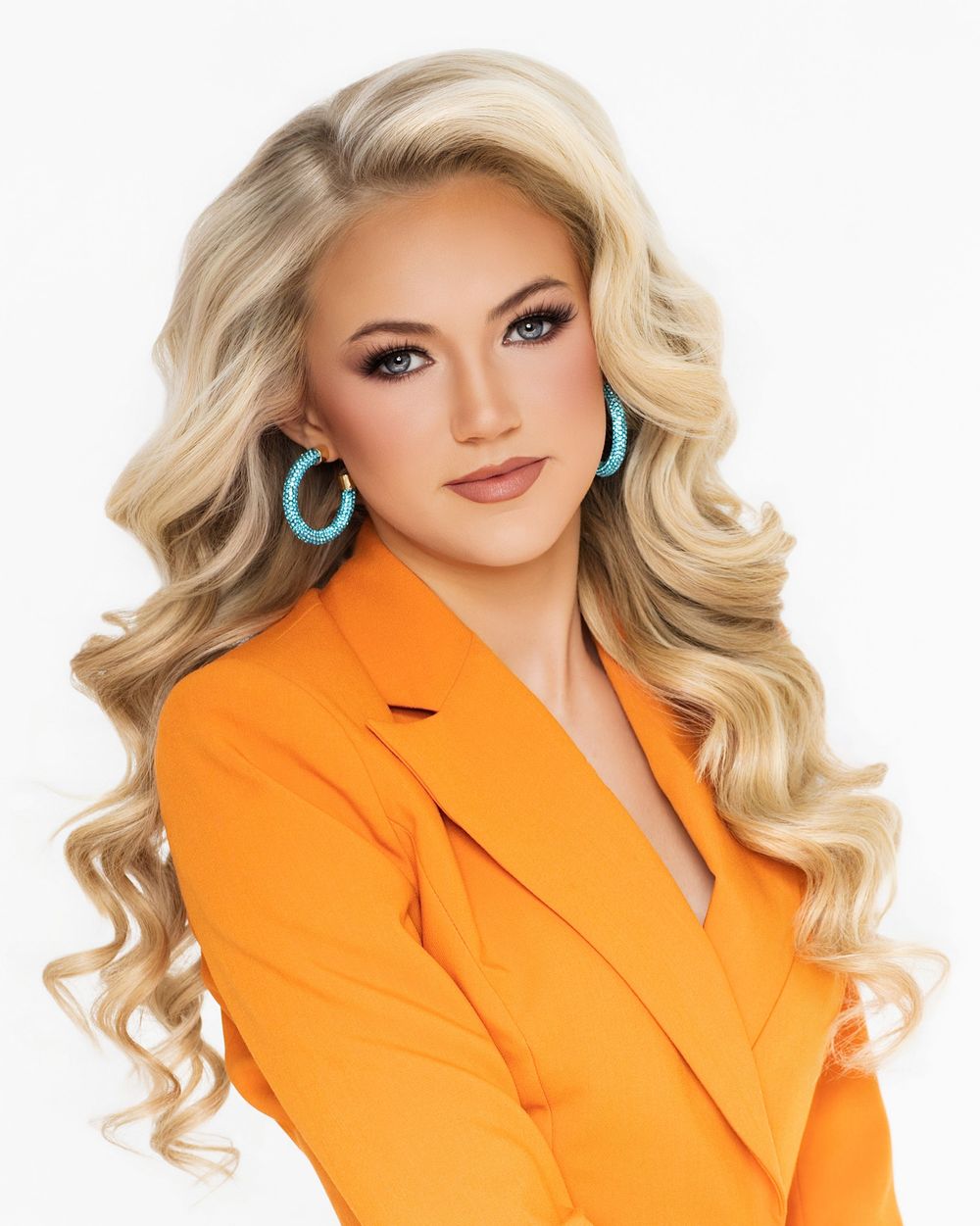 Professional portrait of a person in a bright orange blazer with blonde wavy hair and turquoise earrings against white background.