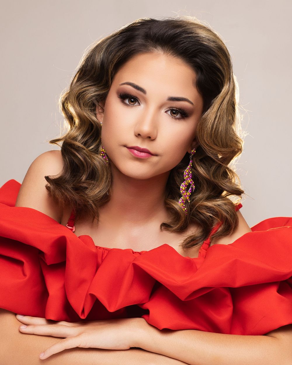 Glamorous portrait of someone in a red ruffled off-shoulder dress with caramel-highlighted wavy hair and elegant makeup.