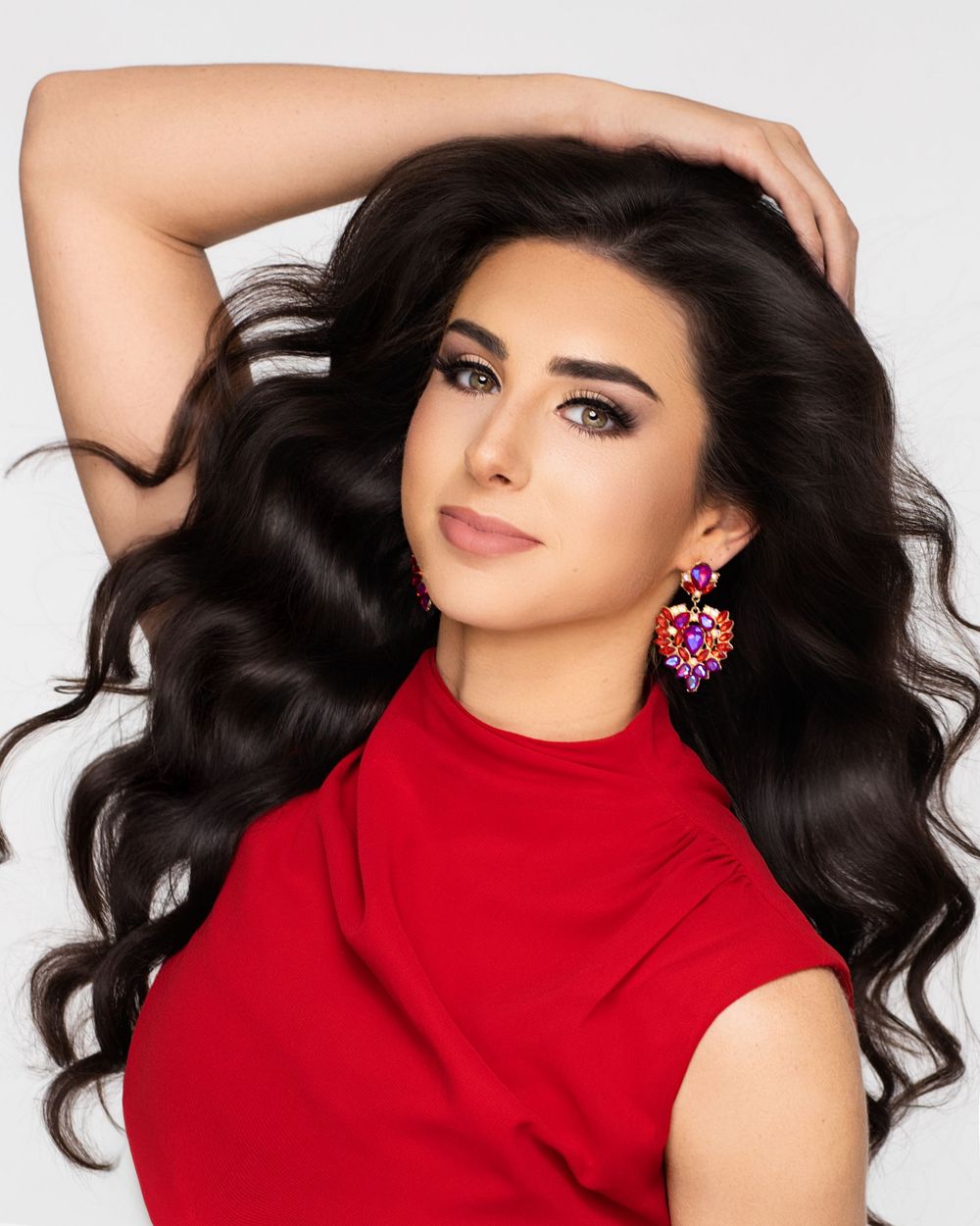 Model wearing a bright red turtleneck dress poses elegantly against white background displaying long dark flowing hair.