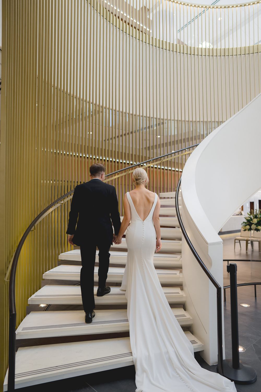 Bride and groom holding hands as they gracefully ascend the grand staircase at the Bradley Symphony Center