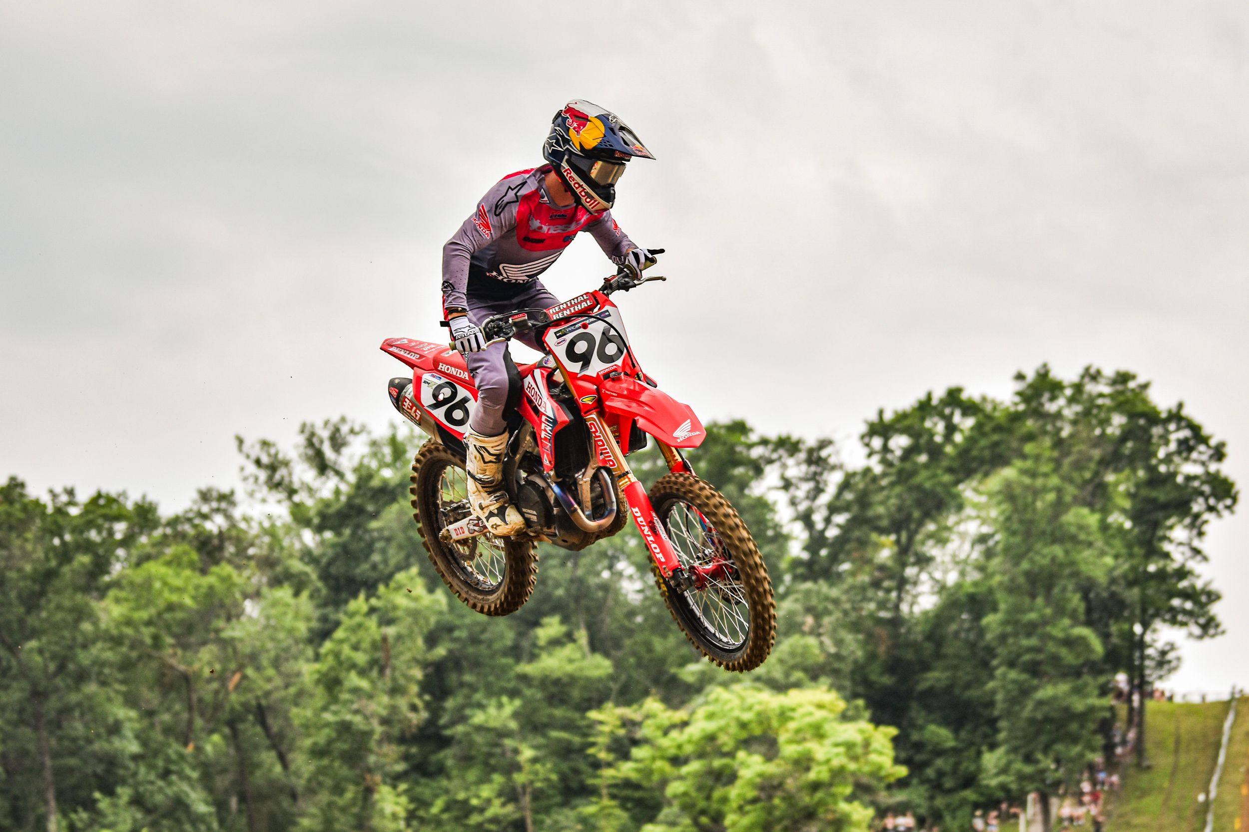 Motocross riders performing high jumps during competition with trees in background.