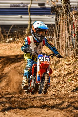 Motocross rider kicks up dirt while racing through wooded course.