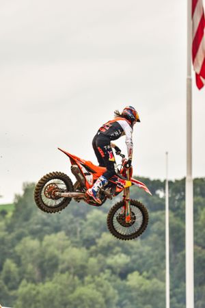 Motocross rider executes dramatic aerial jump with American flags visible in background.