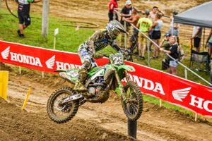 Dirt bike racer navigates muddy track during Honda-sponsored motocross competition.