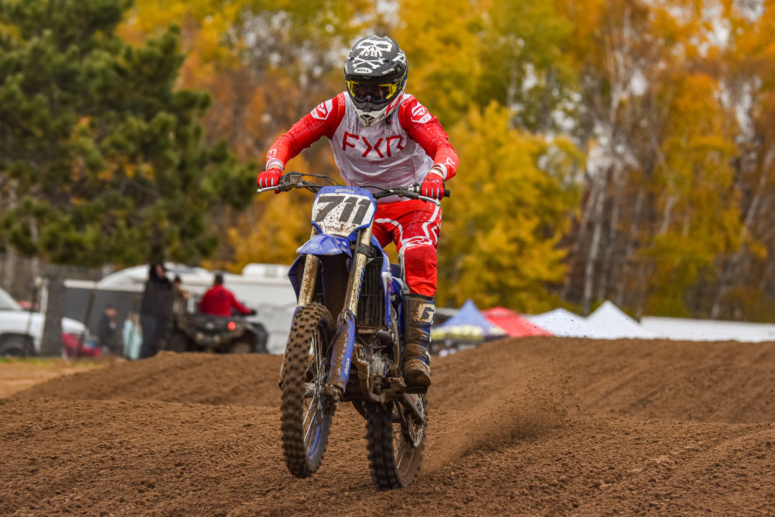 Dirt bike riders racing through autumn landscape with golden foliage.
