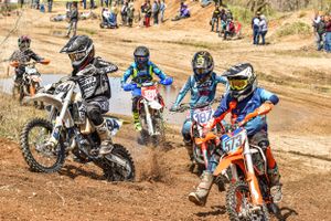 Motocross riders racing through dirt track during competitive outdoor event.