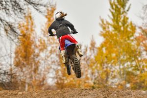 Motocross riders soaring through air during dirt bike competition with autumn trees.