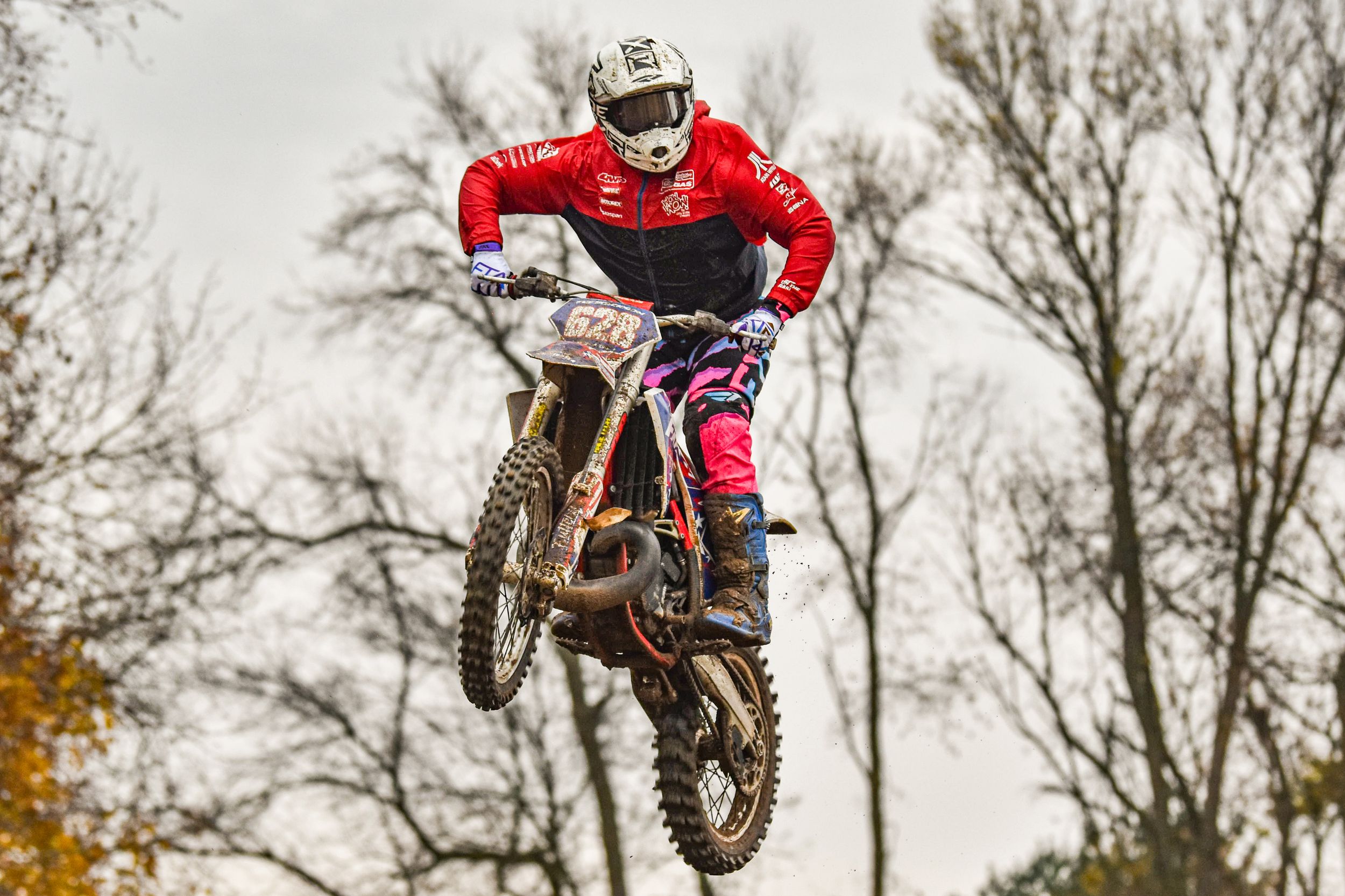 Dirt bike racers catching air during motocross competition on cloudy day.