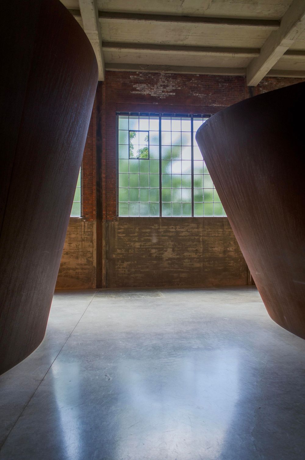 Interior view of an empty industrial space with exposed brick walls and sunlight streaming through high windows.