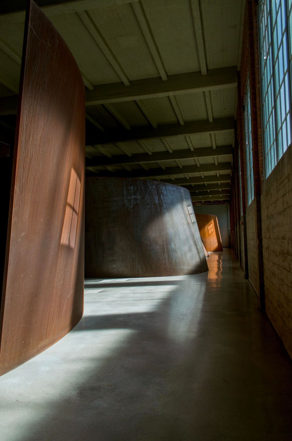 Dark warehouse interior with dramatic shadows cast by natural light filtering through large windows.