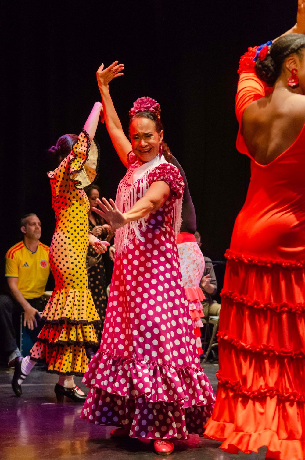 Flamenco dancers in vibrant polka dot dresses perform on stage, with the lead dancer in a red and white gown.