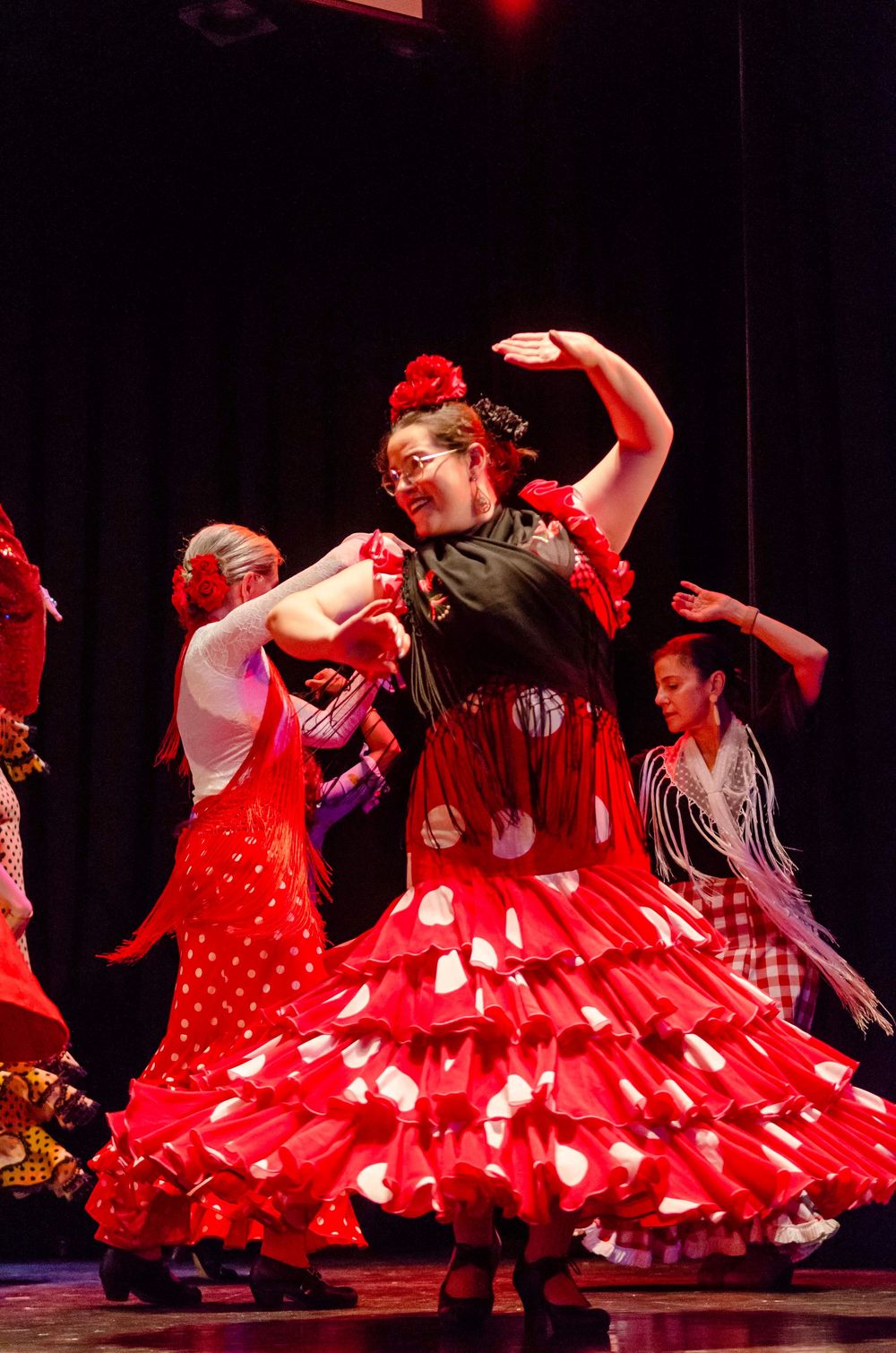Flamenco dancers performing on stage in vibrant red polka dot dresses with ruffled skirts under dramatic stage lighting.