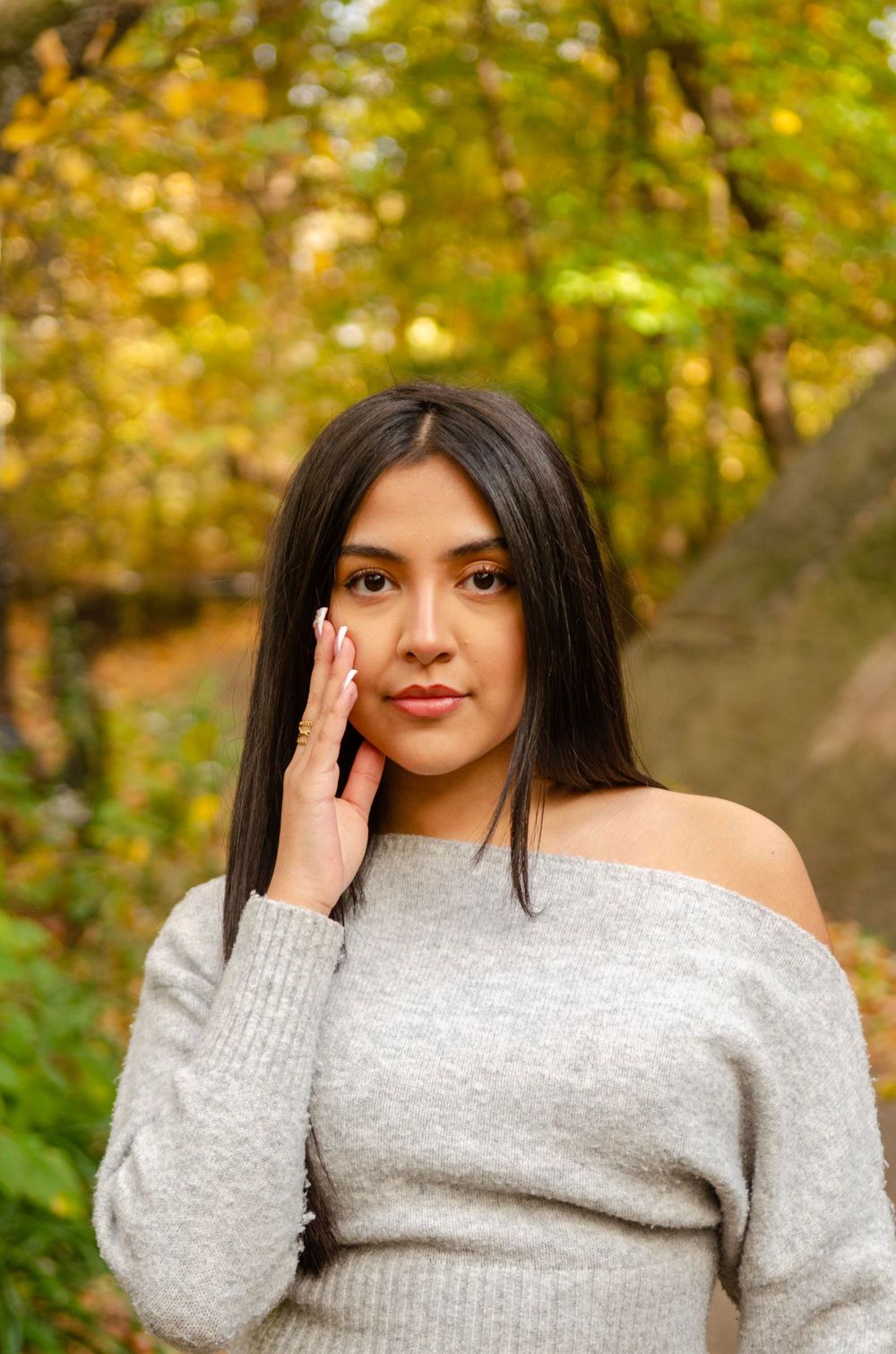 A person wearing a cozy gray sweater poses against a vibrant autumn forest background with golden foliage.