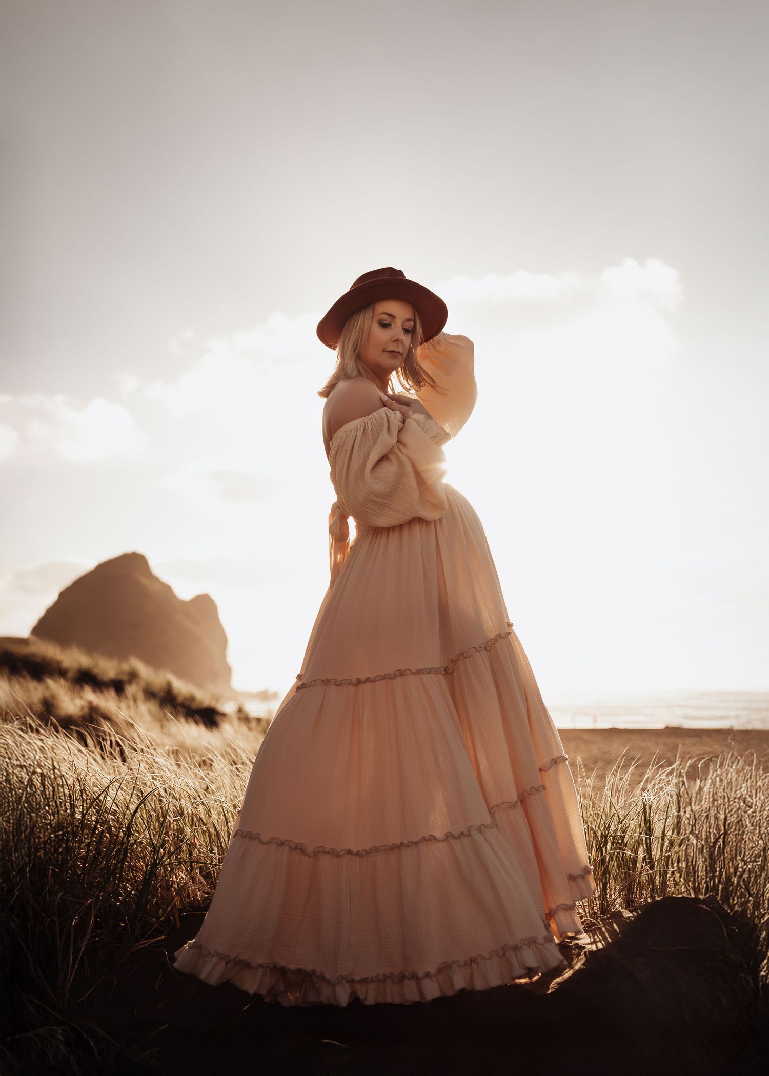 Pregnant woman in lace robe holding her belly with both hands in soft natural light.