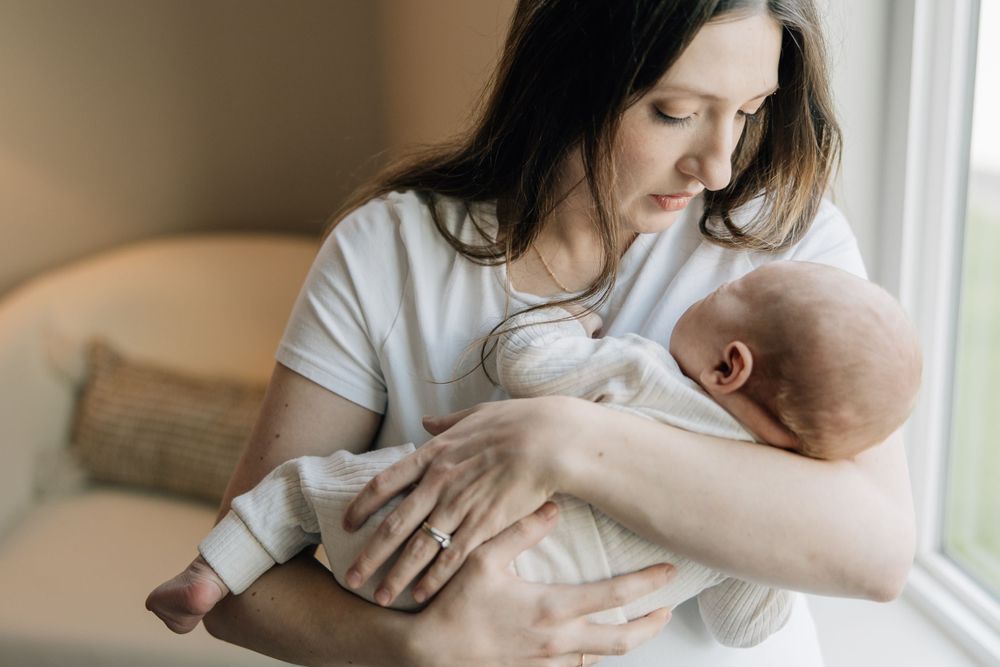 Gentle moment of parent cradling sleeping baby near window with natural light.
