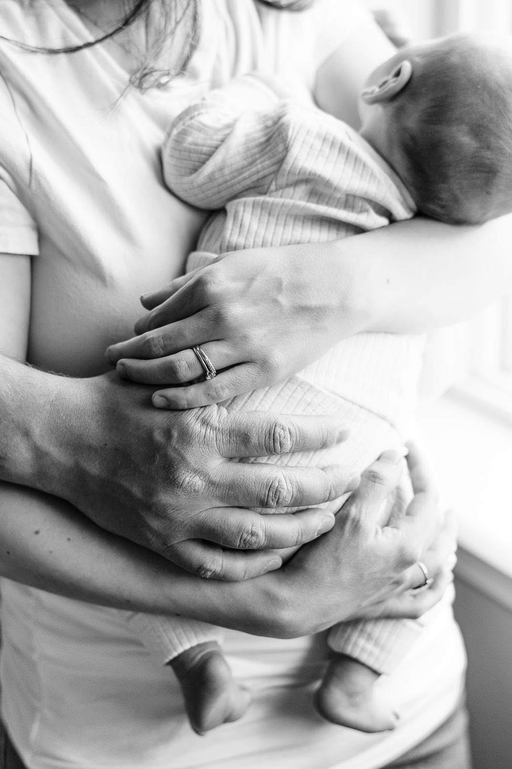 Black and white close-up of hands tenderly holding sleeping baby in white clothing.