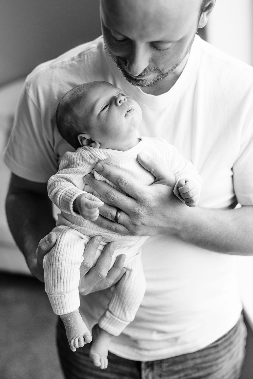 Intimate black and white portrait of parent holding newborn baby in white onesie.