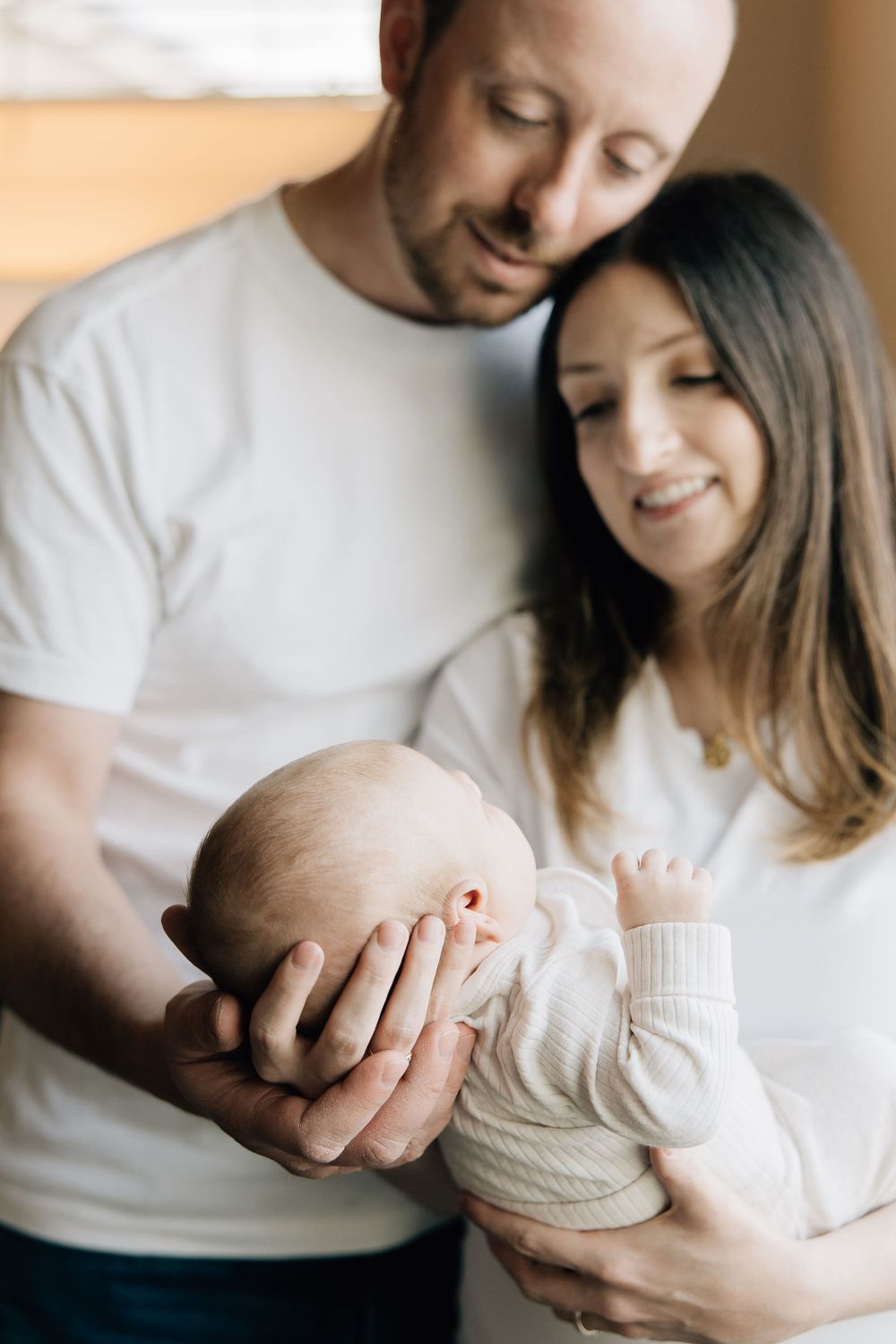 A tender family moment as parents cradle their newborn baby in soft natural lighting.