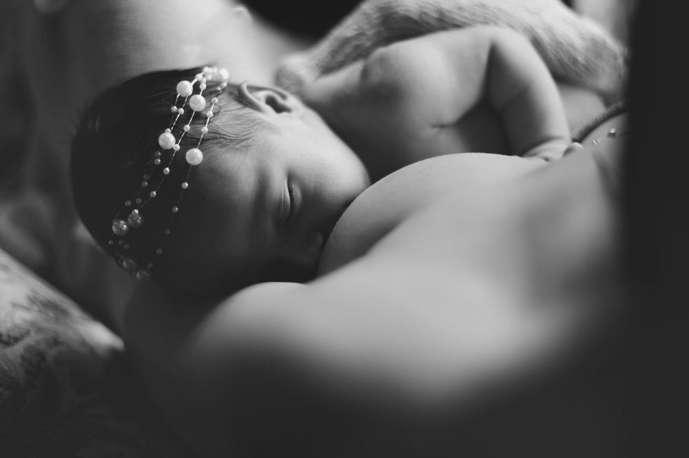 Black and white portrait of sleeping infant wearing delicate headband in moody lighting.