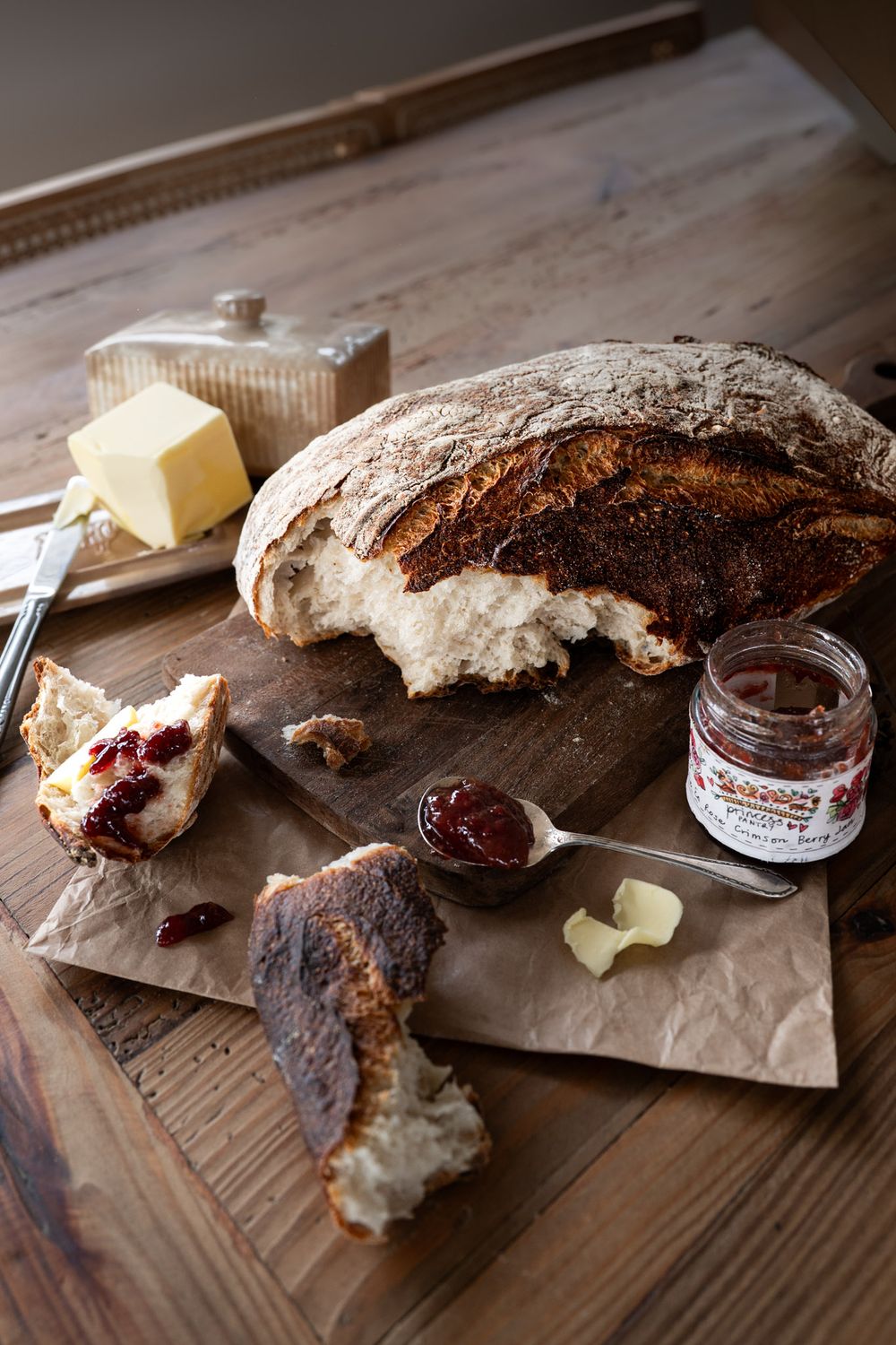 Rustic bread loaf with butter and jam spread on wooden table with artisanal breakfast setup.