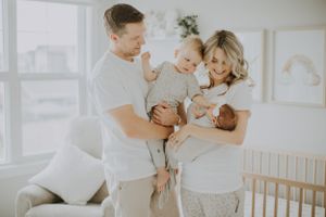 A family shares a tender moment together in a bright, white nursery room with natural lighting coming through the window.