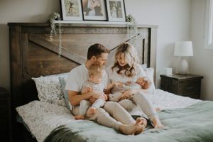 Family relaxing together on bed with floral bedding and rustic wooden headboard in cozy bedroom setting.