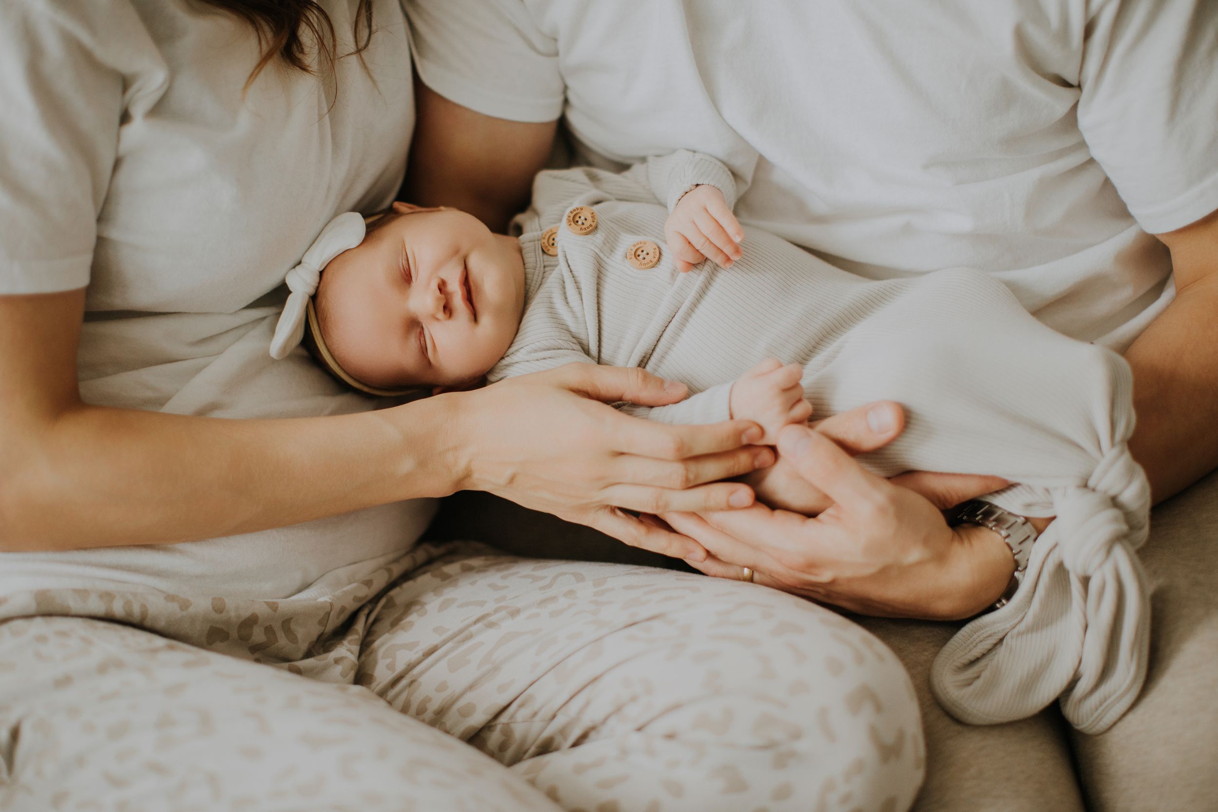 Gentle hands lovingly comfort a small baby lying on soft beige bedding in a tender family moment.