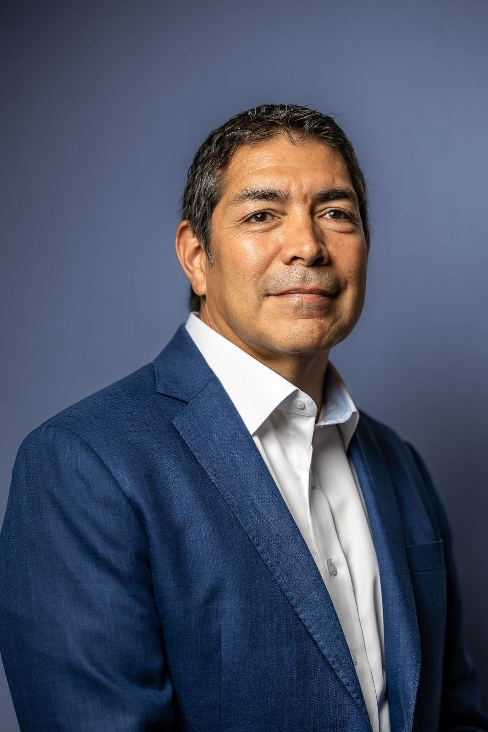Professional portrait series showing different angles of person in navy suit and white dress shirt against blue backdrop.