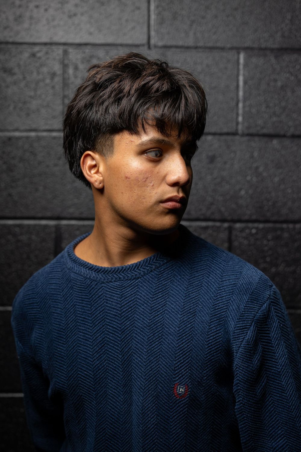 A person wearing a navy blue sweater poses against a dark wall in a series of profile shots.