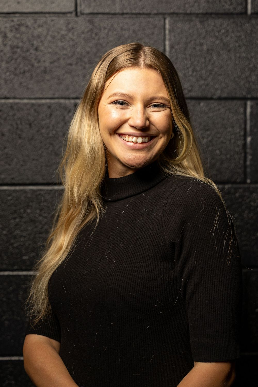 Portrait of someone wearing a black turtleneck sweater against a dark brick wall background.