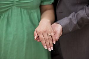 Engaged couples' hands with her Engagement ring, she is wearing a green dress and he is in a grey suit..