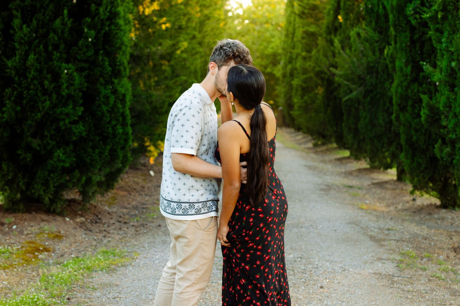 Couple walking together on tree-lined path during outdoor photo session.