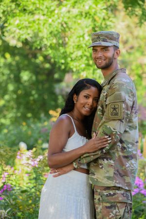 A couple poses in a garden setting with one person wearing military fatigues.