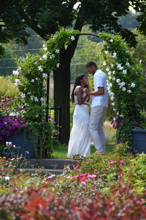 A romantic garden scene with two people embracing under a floral arch surrounded by colorful flowers.