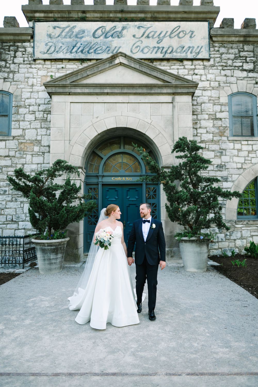 Wedding party in formal attire with bridesmaids wearing bright blue dresses standing on grass with trees in background.