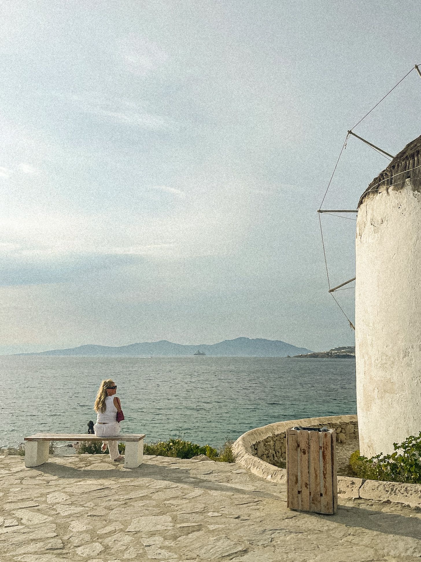 A scenic view of a white windmill by the Mediterranean Sea with mountains in the distance.