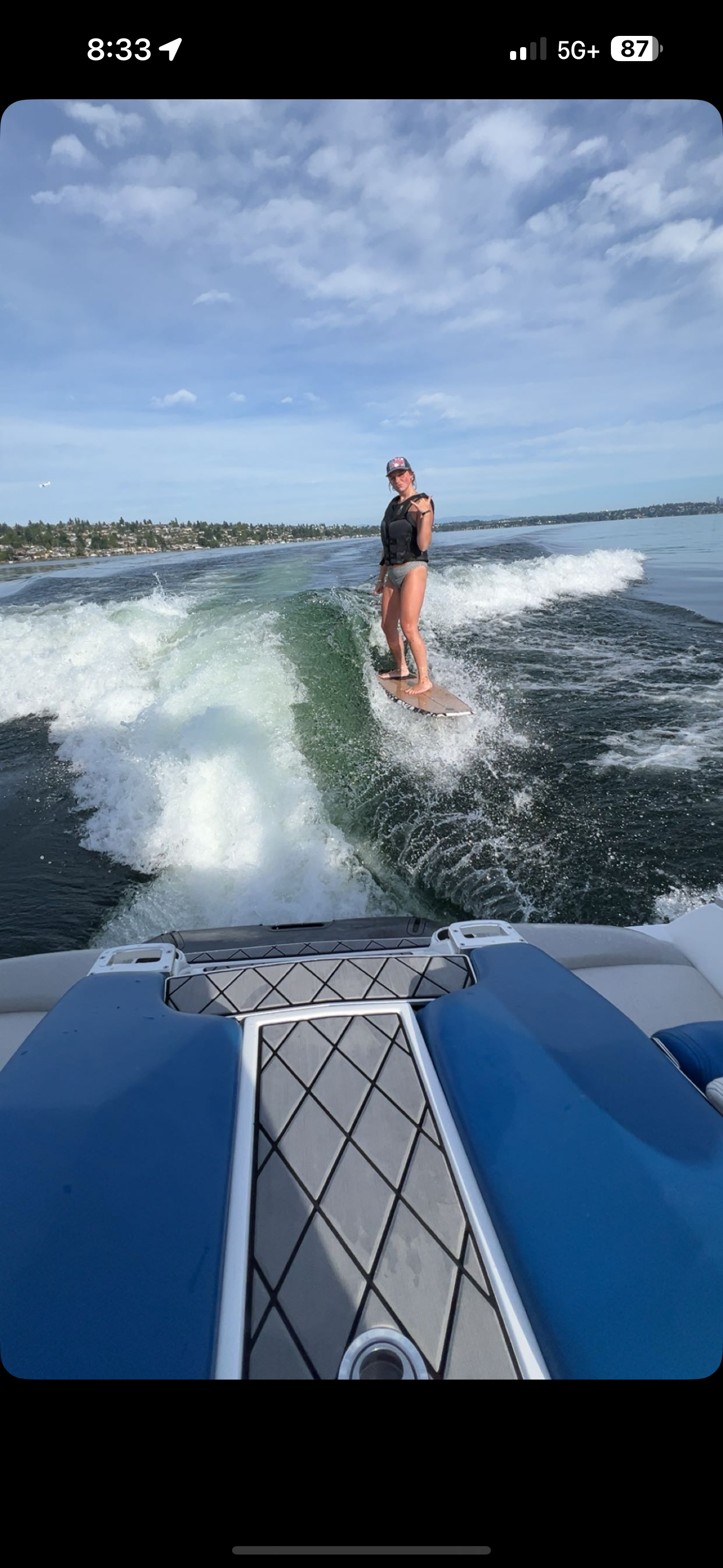 A wakeboarder performs aerial maneuvers behind a boat on calm blue waters under a bright sunny sky.