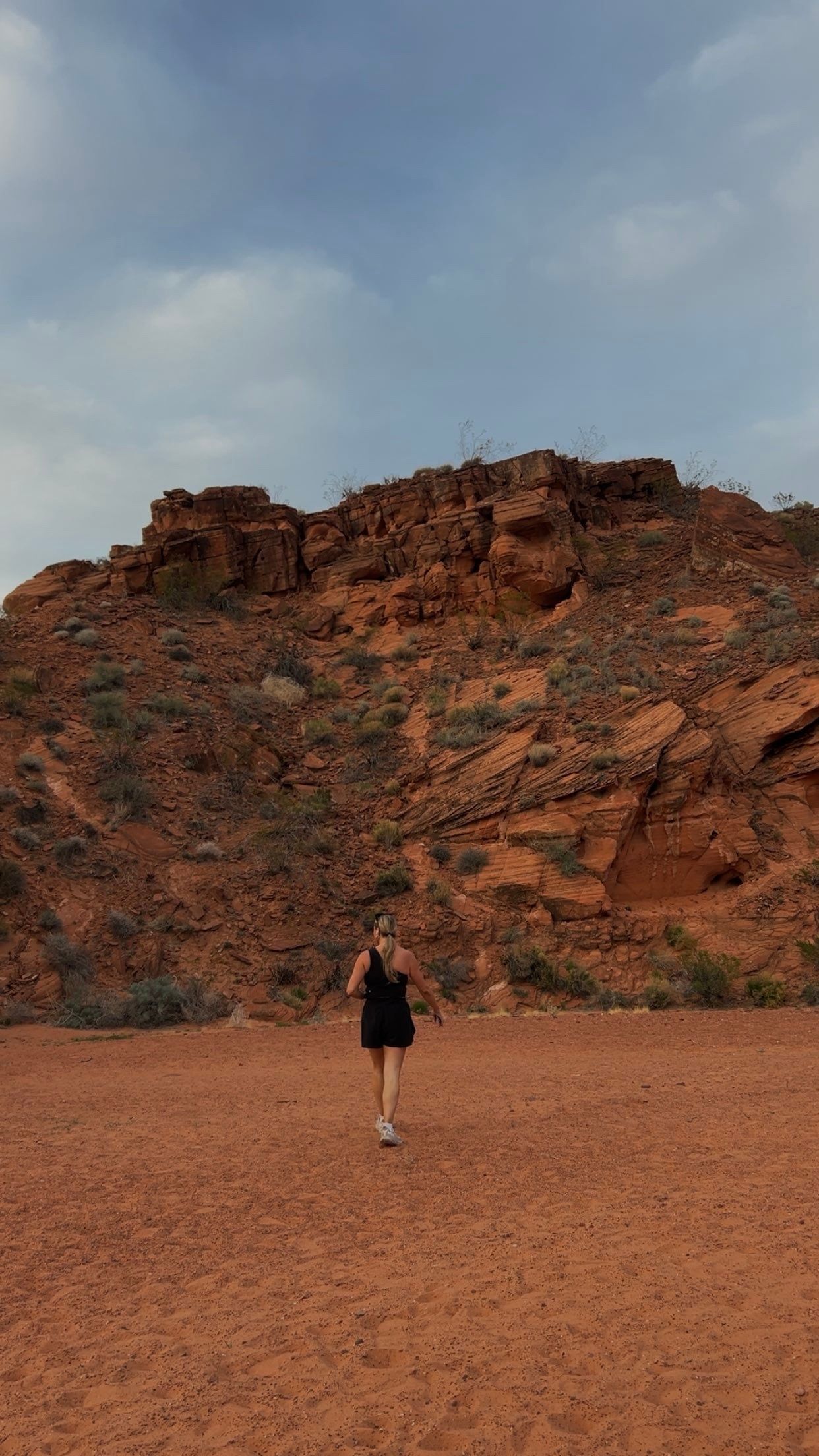 A distant figure in black stands against dramatic red rock formations in a desert landscape.