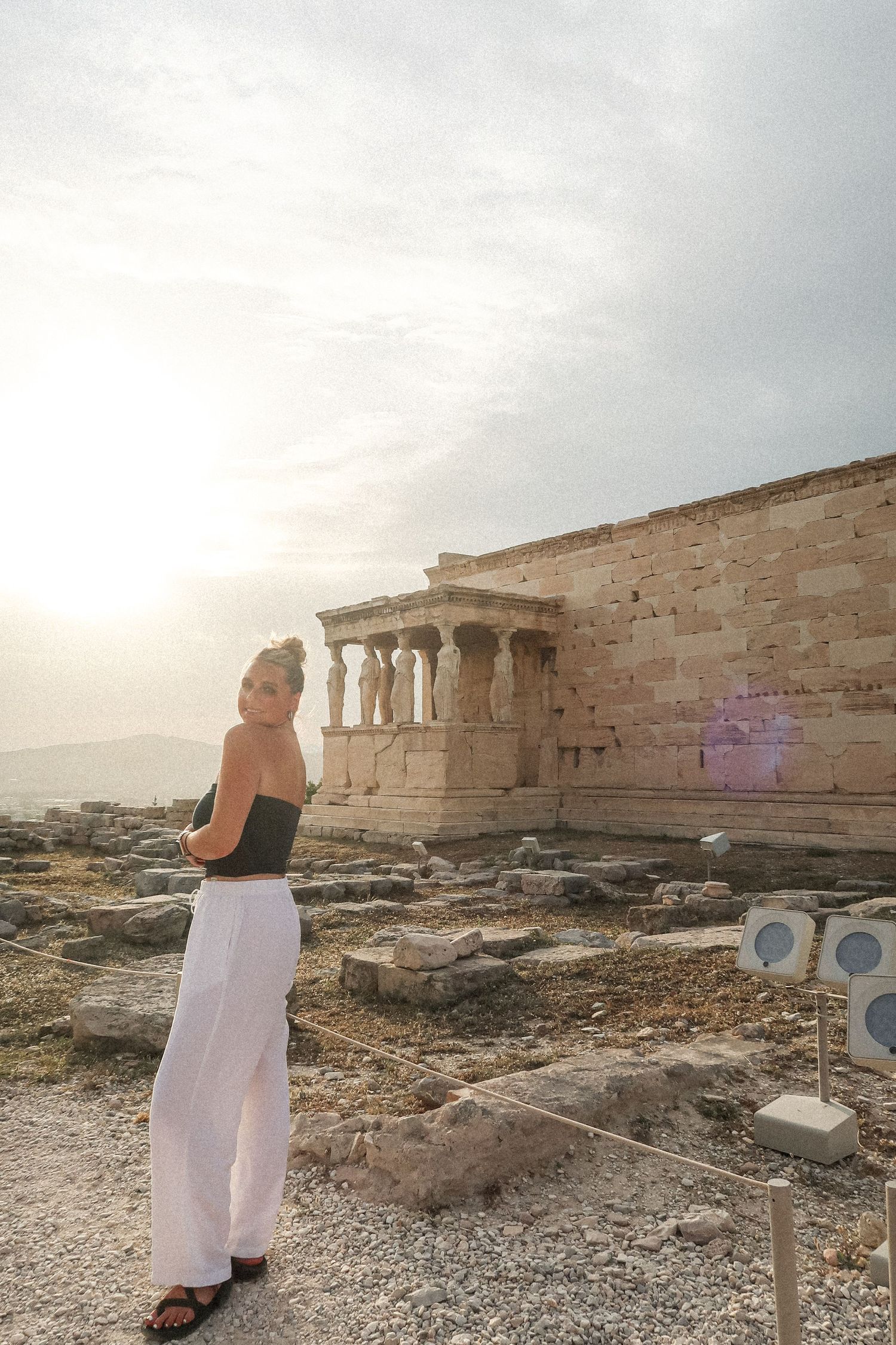 A scenic view at the Acropolis with ancient Greek ruins and columns at sunset.