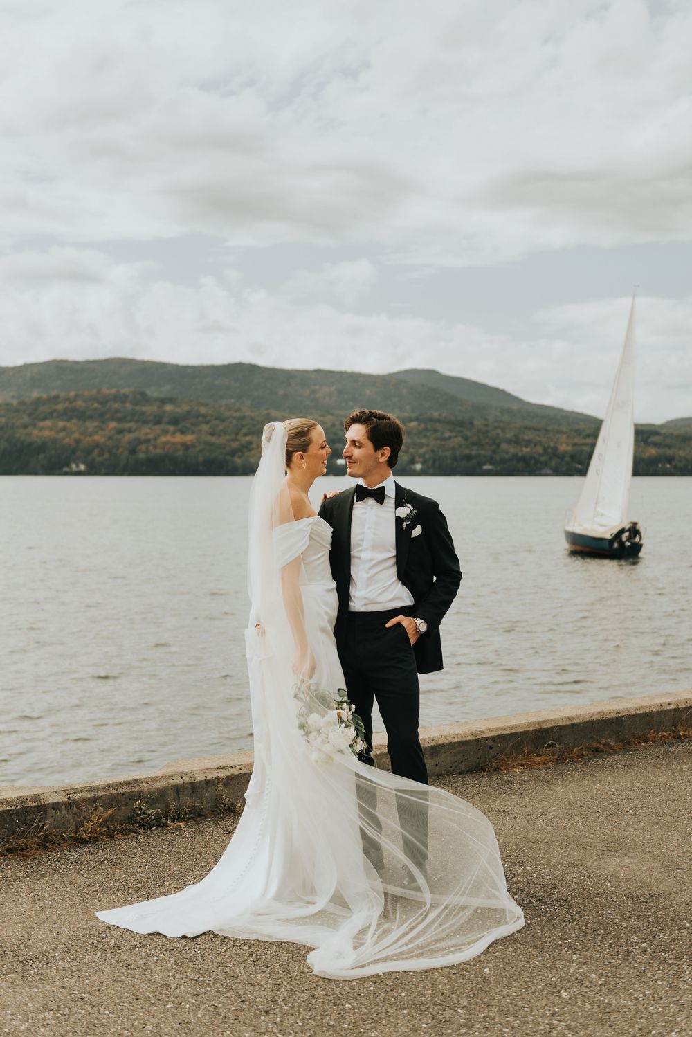 A couple shares an intimate moment by a lake with mountains in the background during their wedding photoshoot.