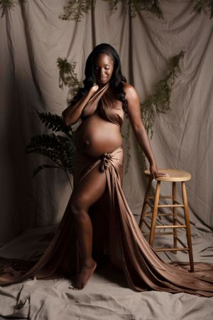 Artistic maternity photo with draped brown fabric and natural elements.