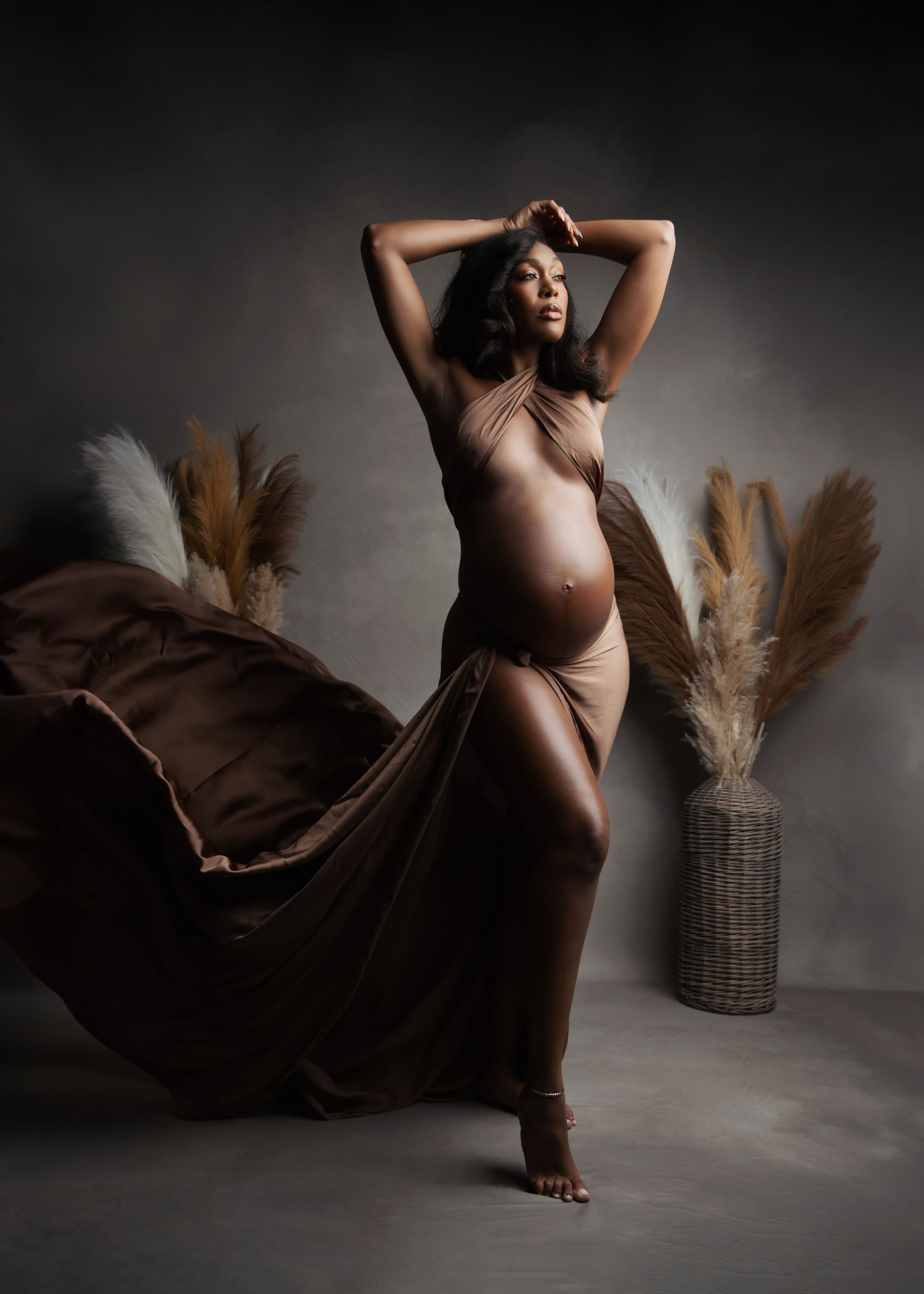 Artistic maternity photo with flowing fabric and pampas grass decor in moody lighting.
