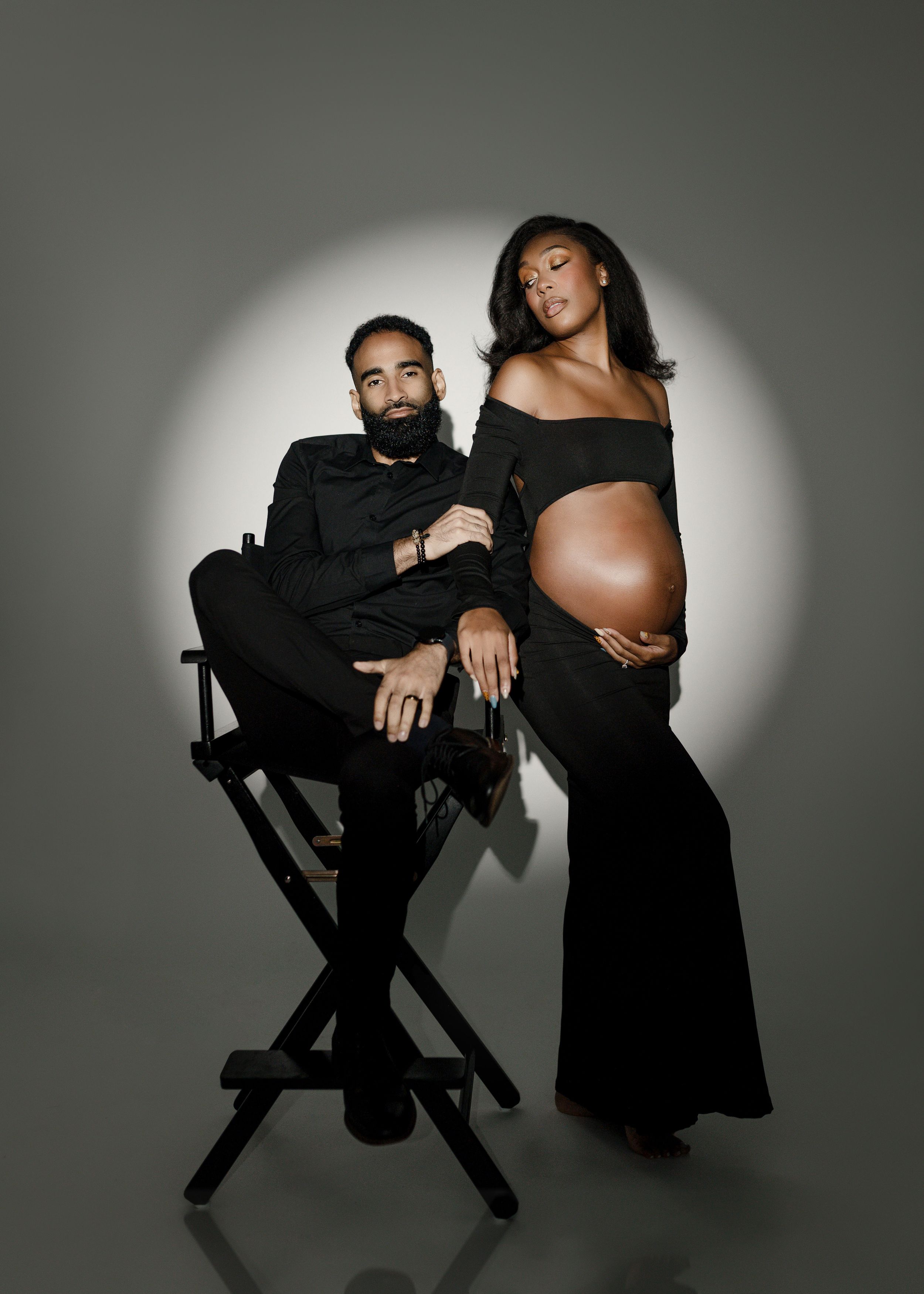 Dramatic maternity photoshoot with couple against grey background with spotlight effect.