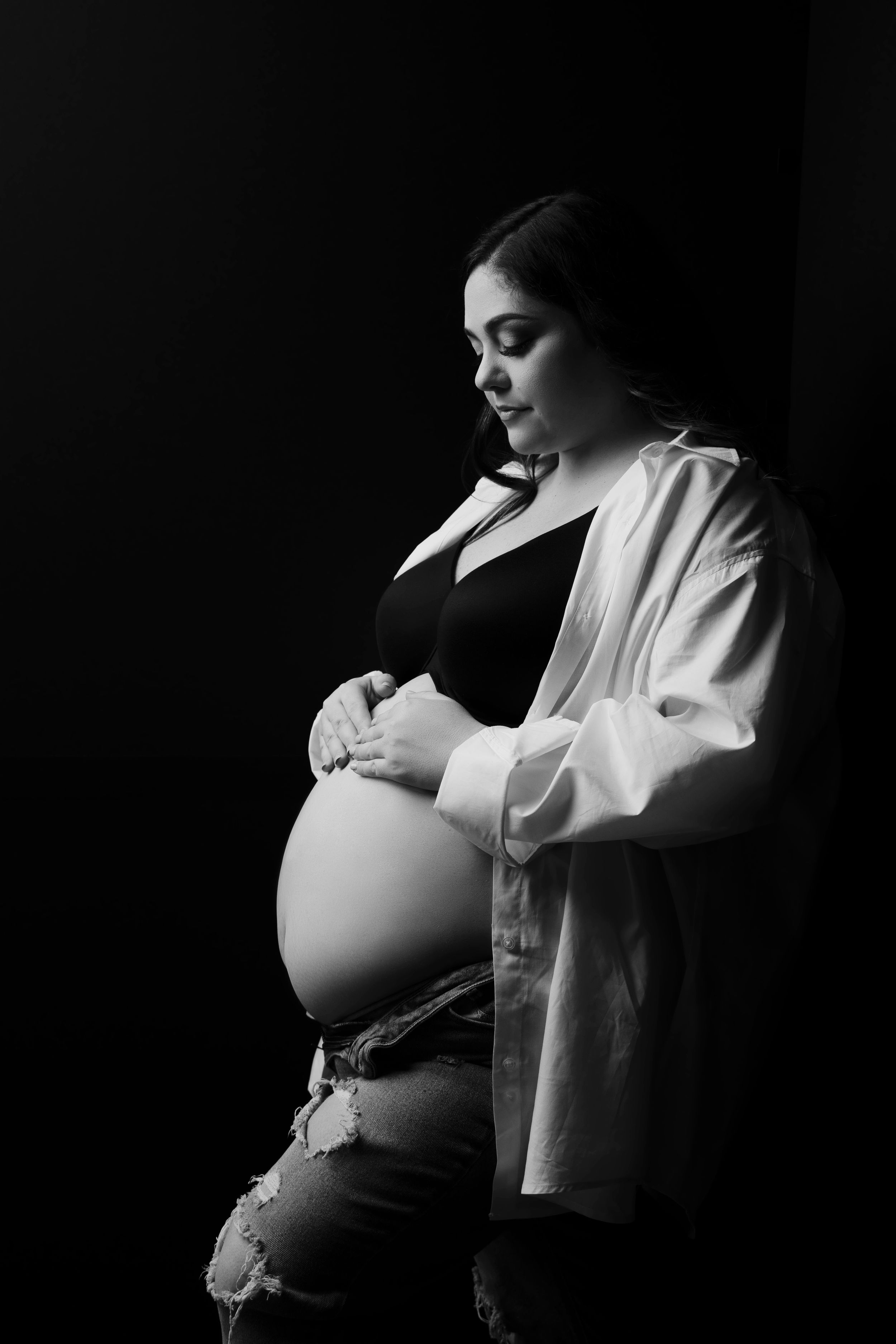 An artistic black and white maternity photo showing an expectant mother in a white shirt.