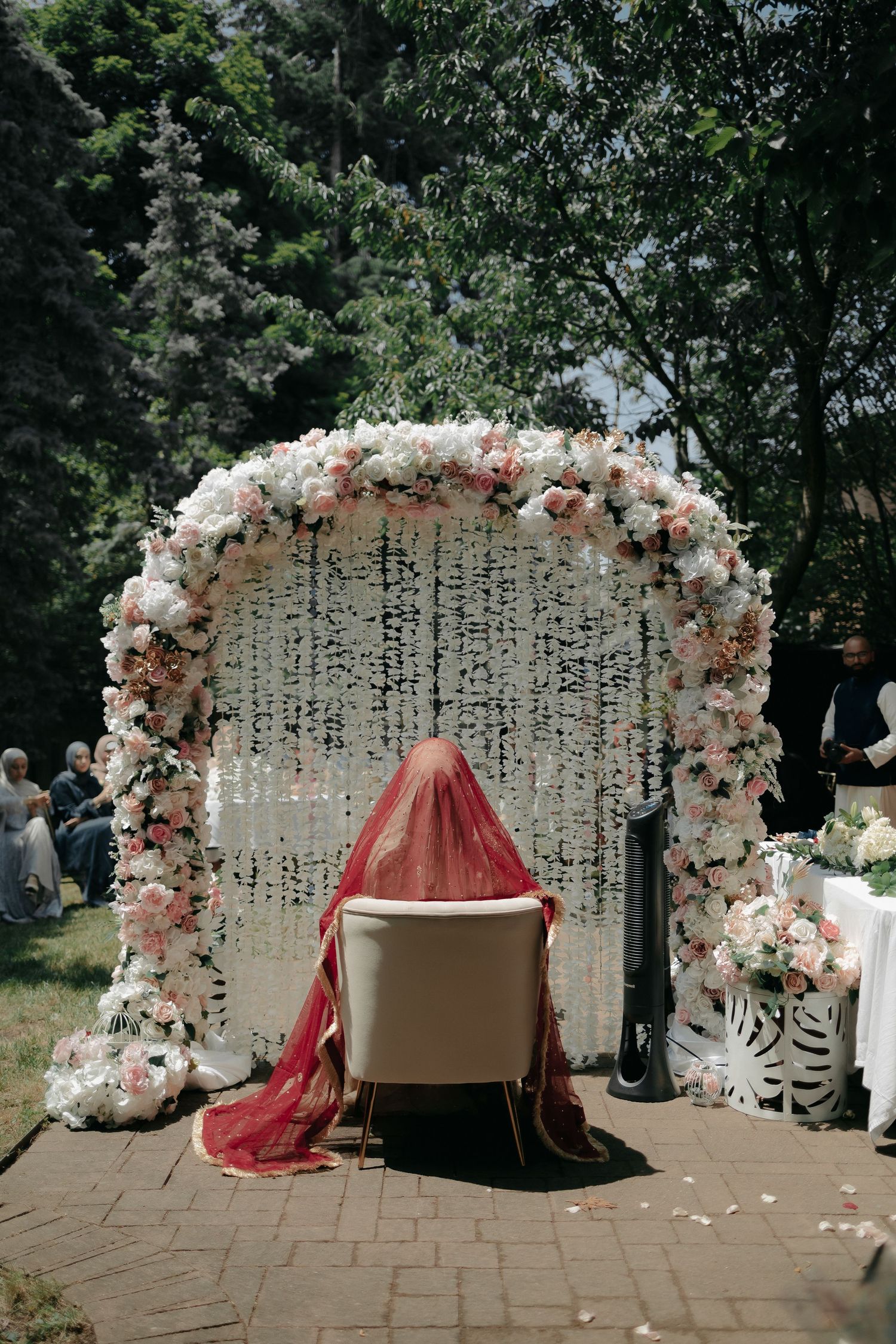 Elegant floral arch with crystal curtains and red draped chair for wedding ceremony.