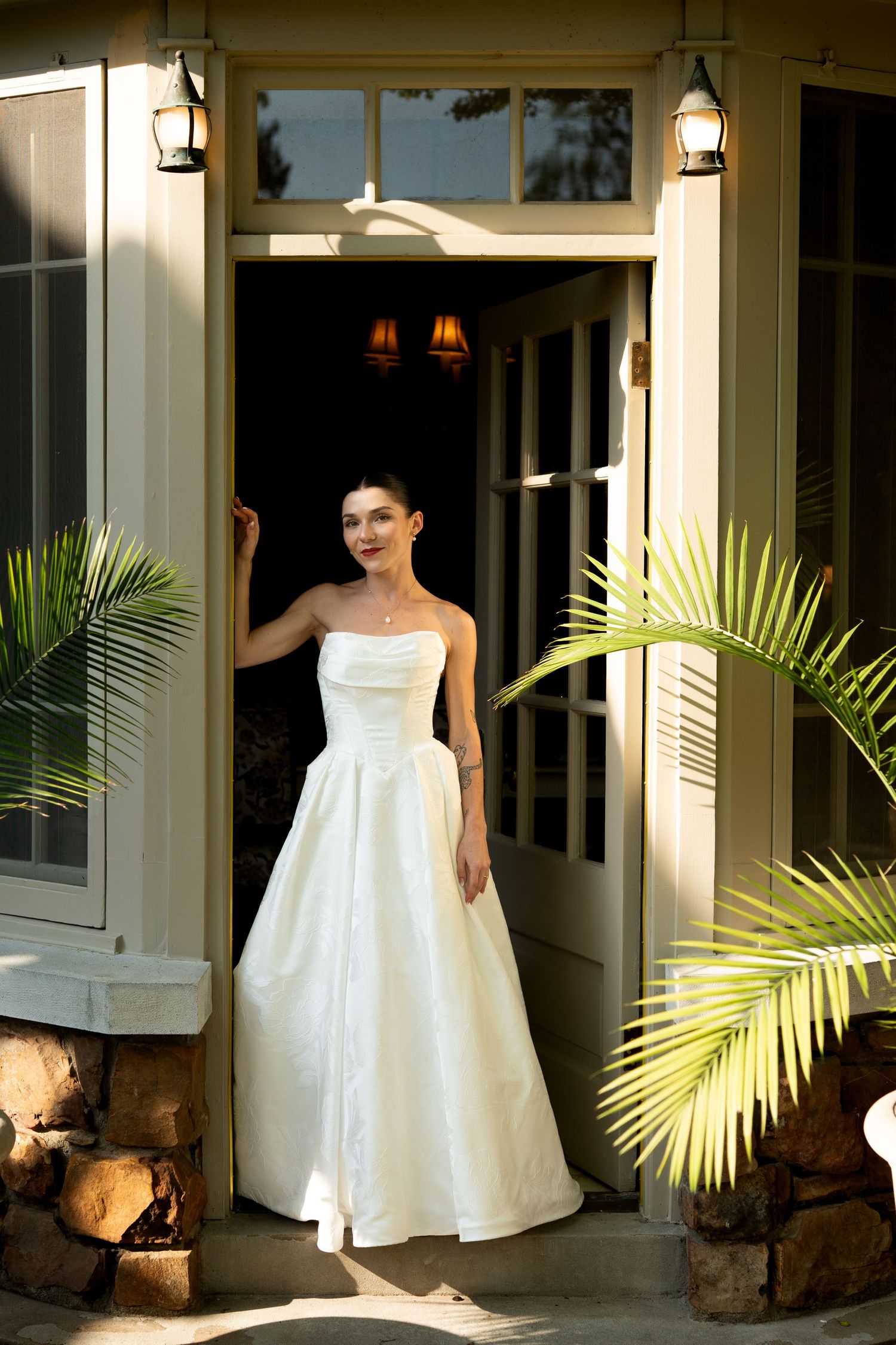 A white wedding dress displayed on a porch with tropical palm fronds.