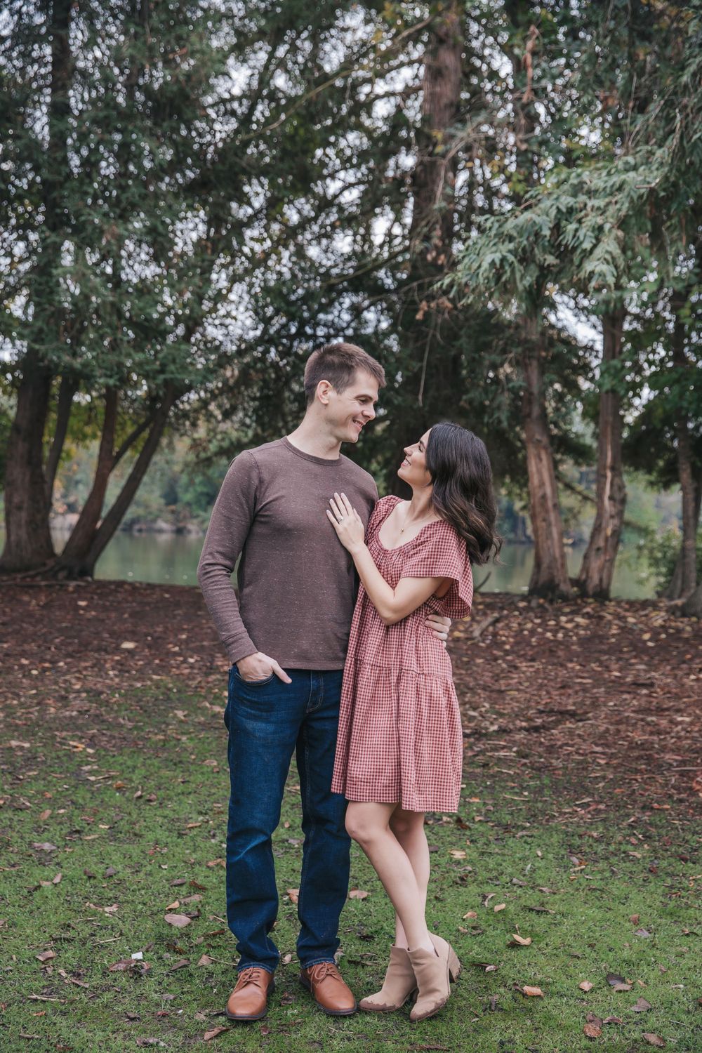 Couple sharing a romantic moment in a lush green park, woman in pink dress, man in brown sweater and jeans.