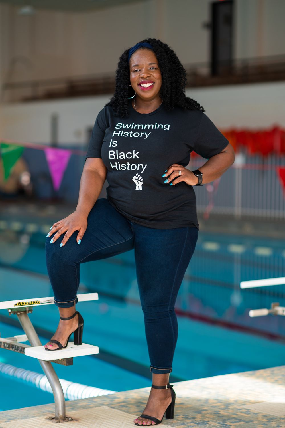 The swim instructor smiles proudly with her foot placed on top of a diving block.
