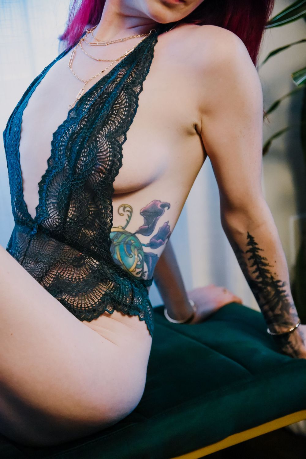 Artistic photo showing dark blue lace bodysuit and arm tattoos against green background.