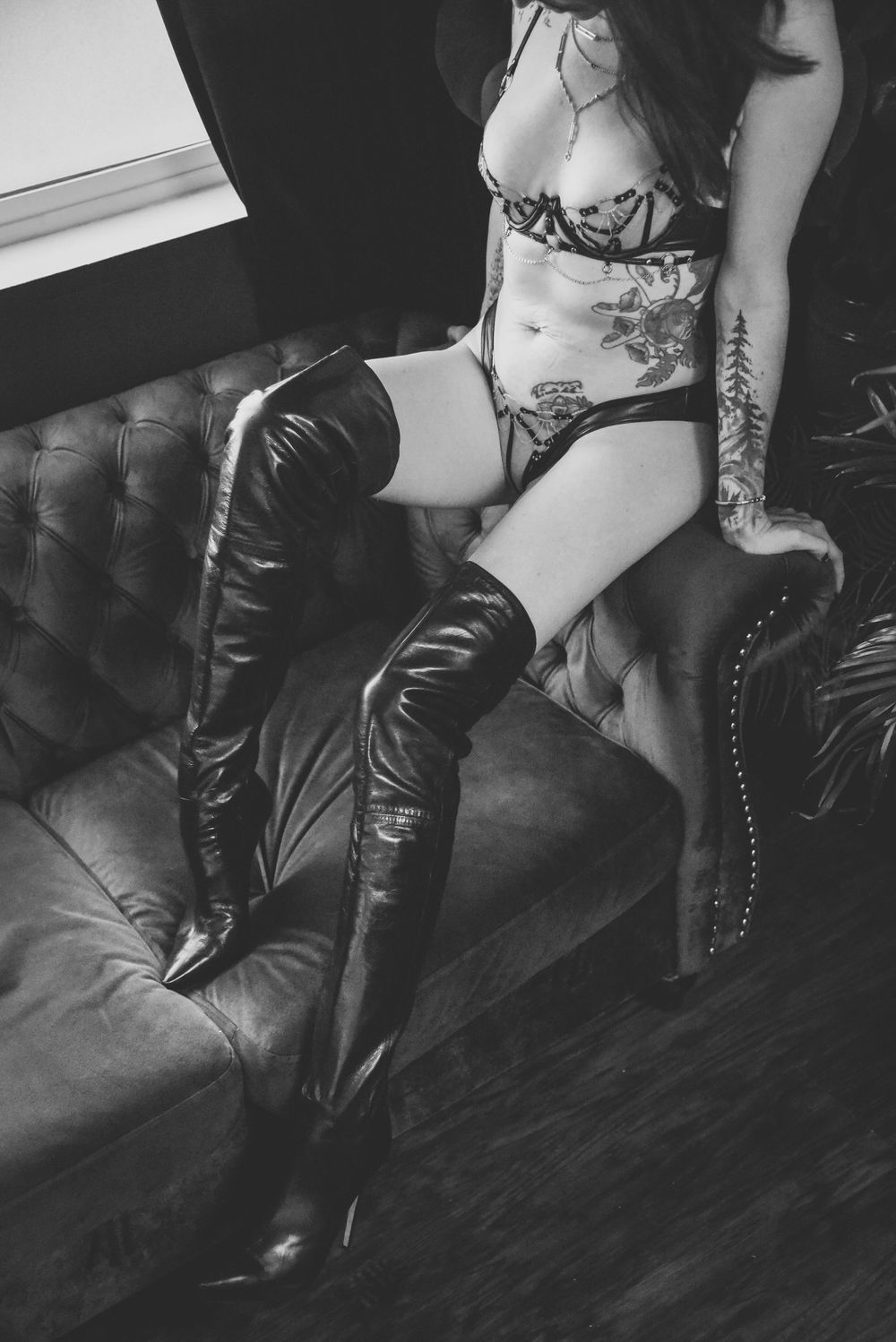 Black and white photo of leather boots and floral lingerie on tufted leather furniture.